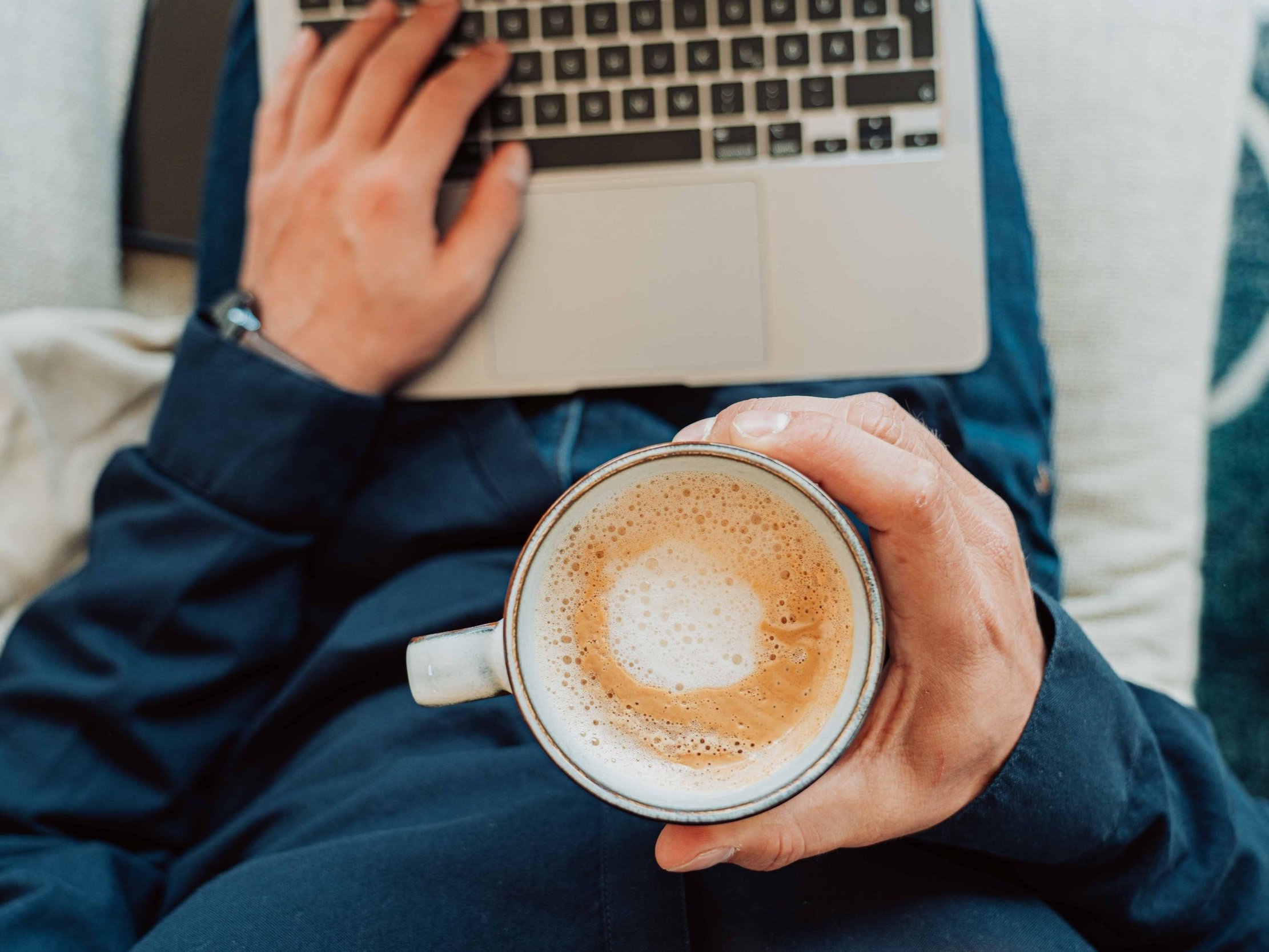 A man sat with his laptop on his lap, enjoying a relaxing coffee break.