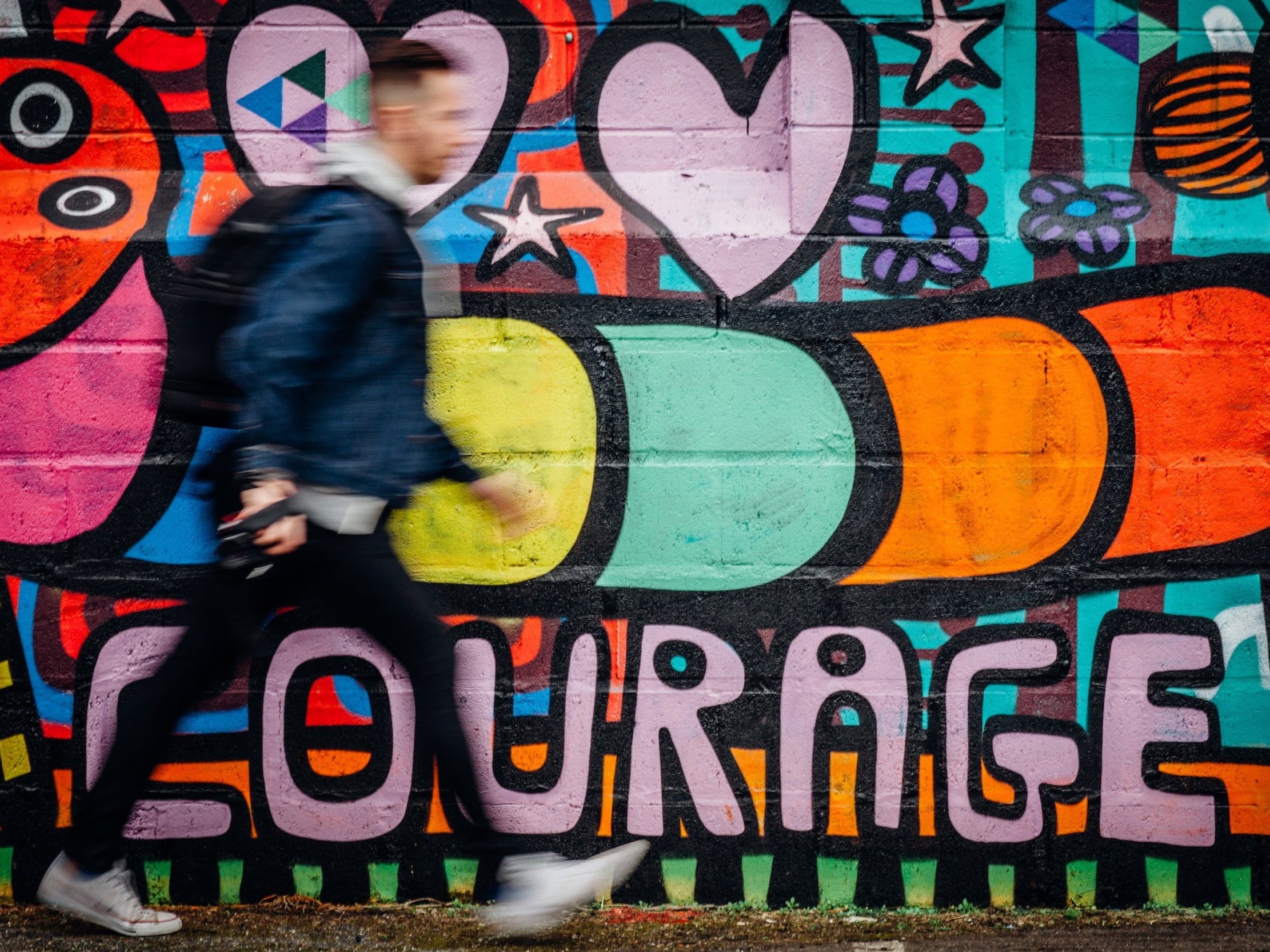 A person walks past a graffiti wall with the words "courage" written on it.