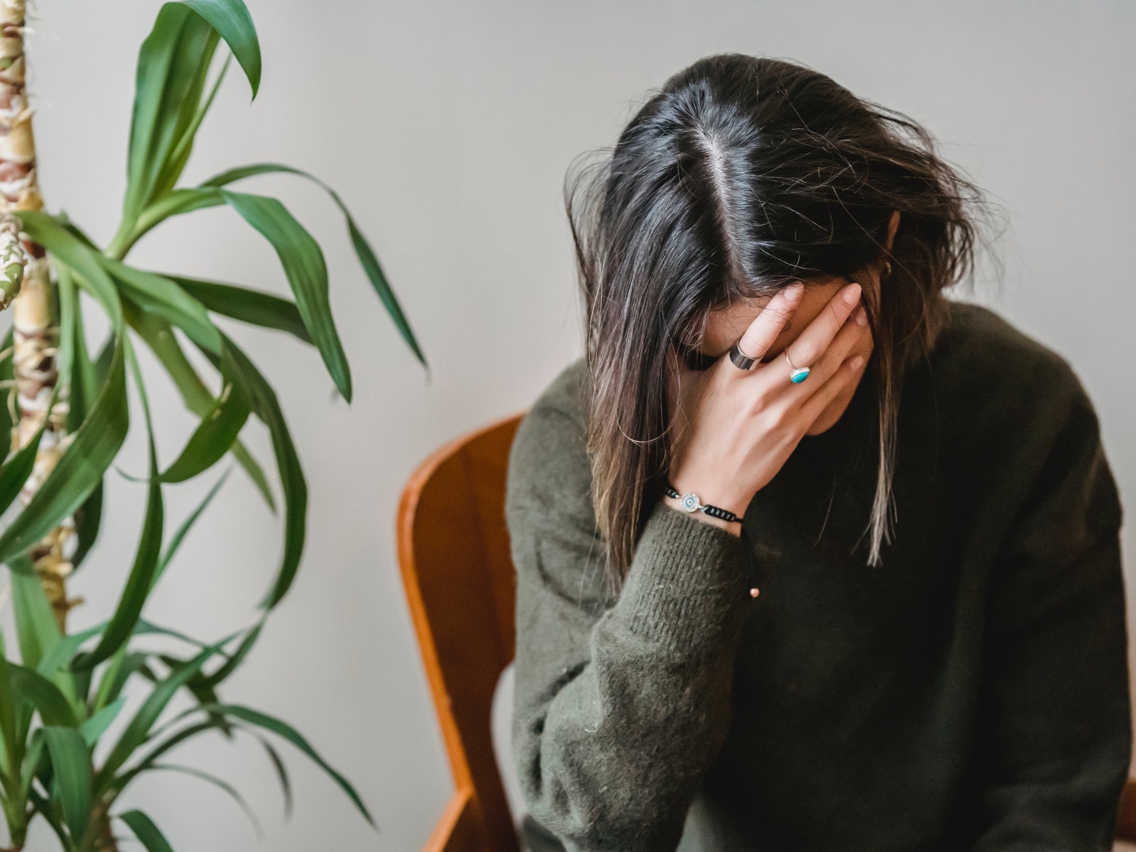 A young woman with her head in her hands, pondering and anxious.