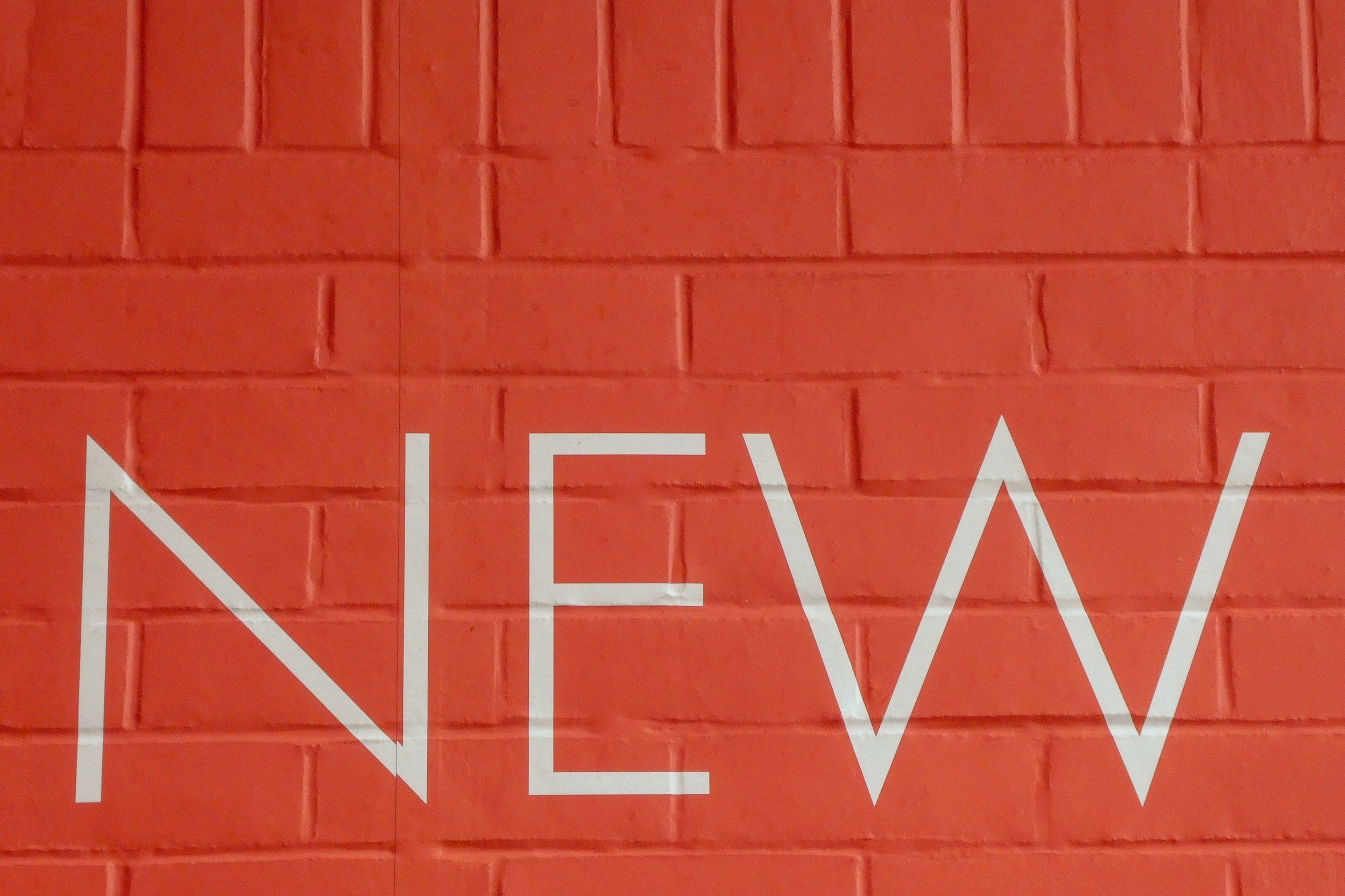 On a vinyl-covered brick wall, the word "New" is written in vinyl.