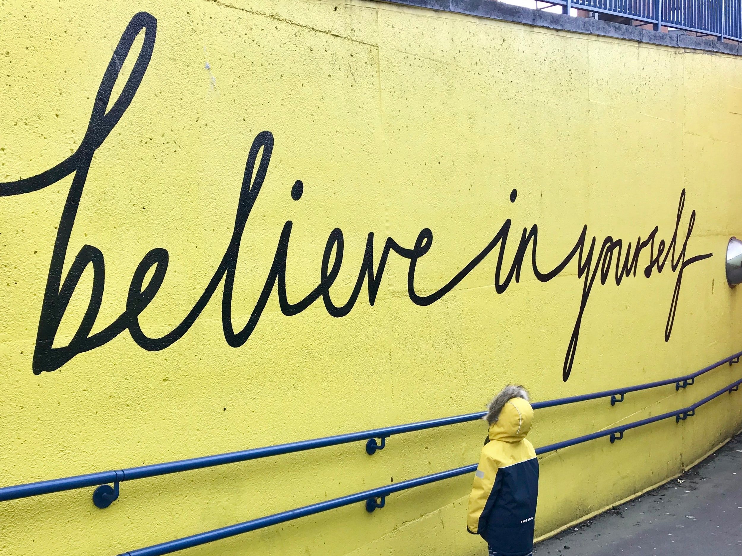 A child examines a mural on a wall with the words "Believe in yourself."