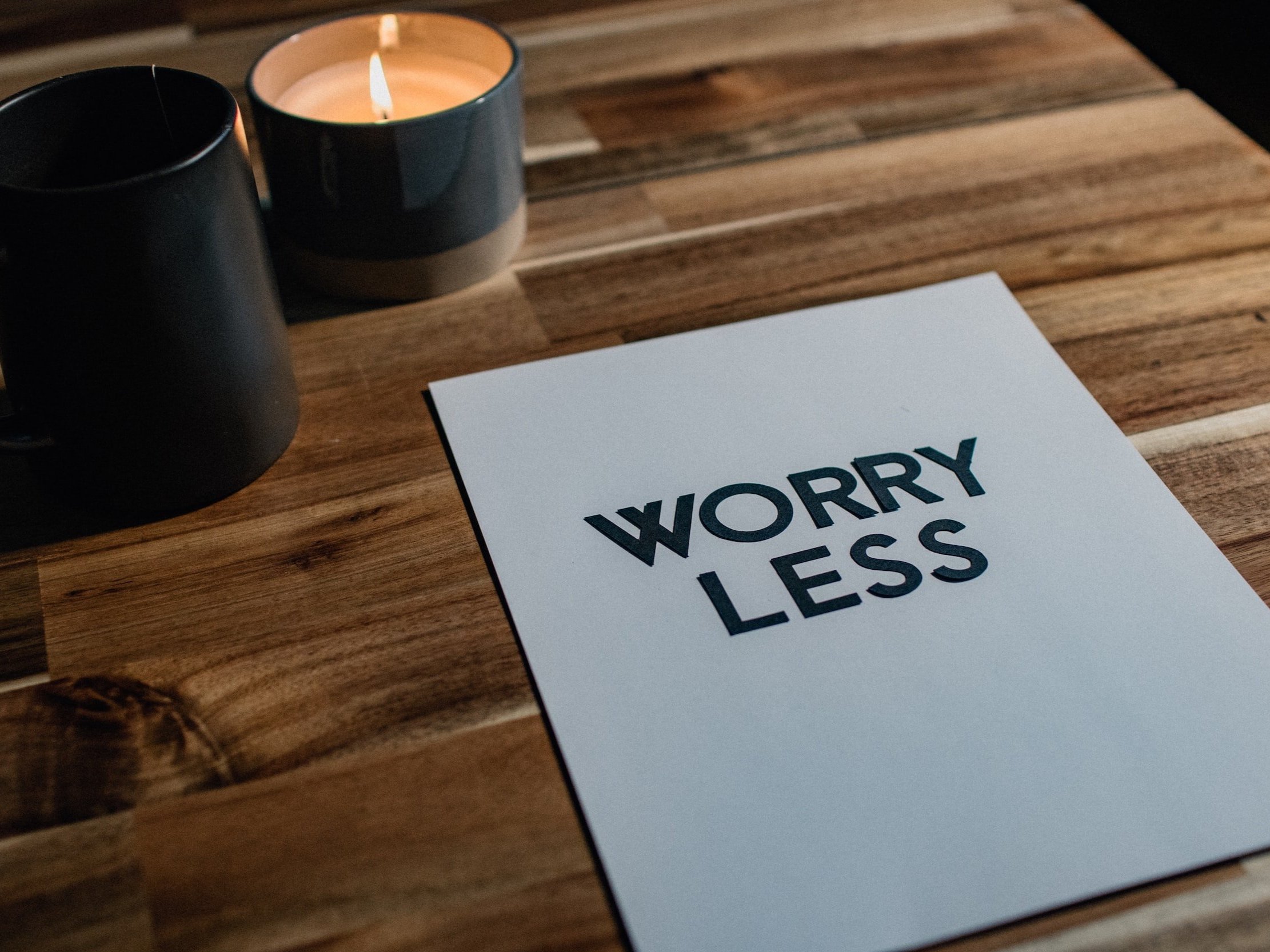 On a wooden surface, the words "worry less" were stuck on a piece of paper next to a lit candle.