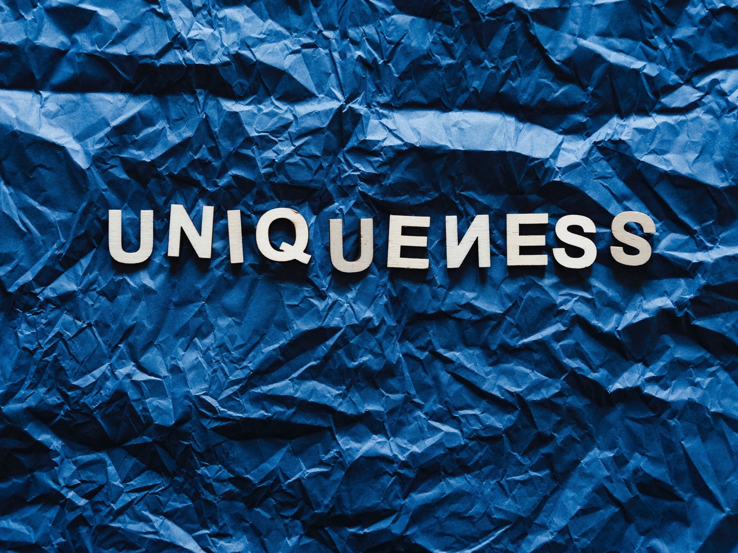 White text on crumpled blue paper misspells the word "uniqueness" by inverting one of the Ns.