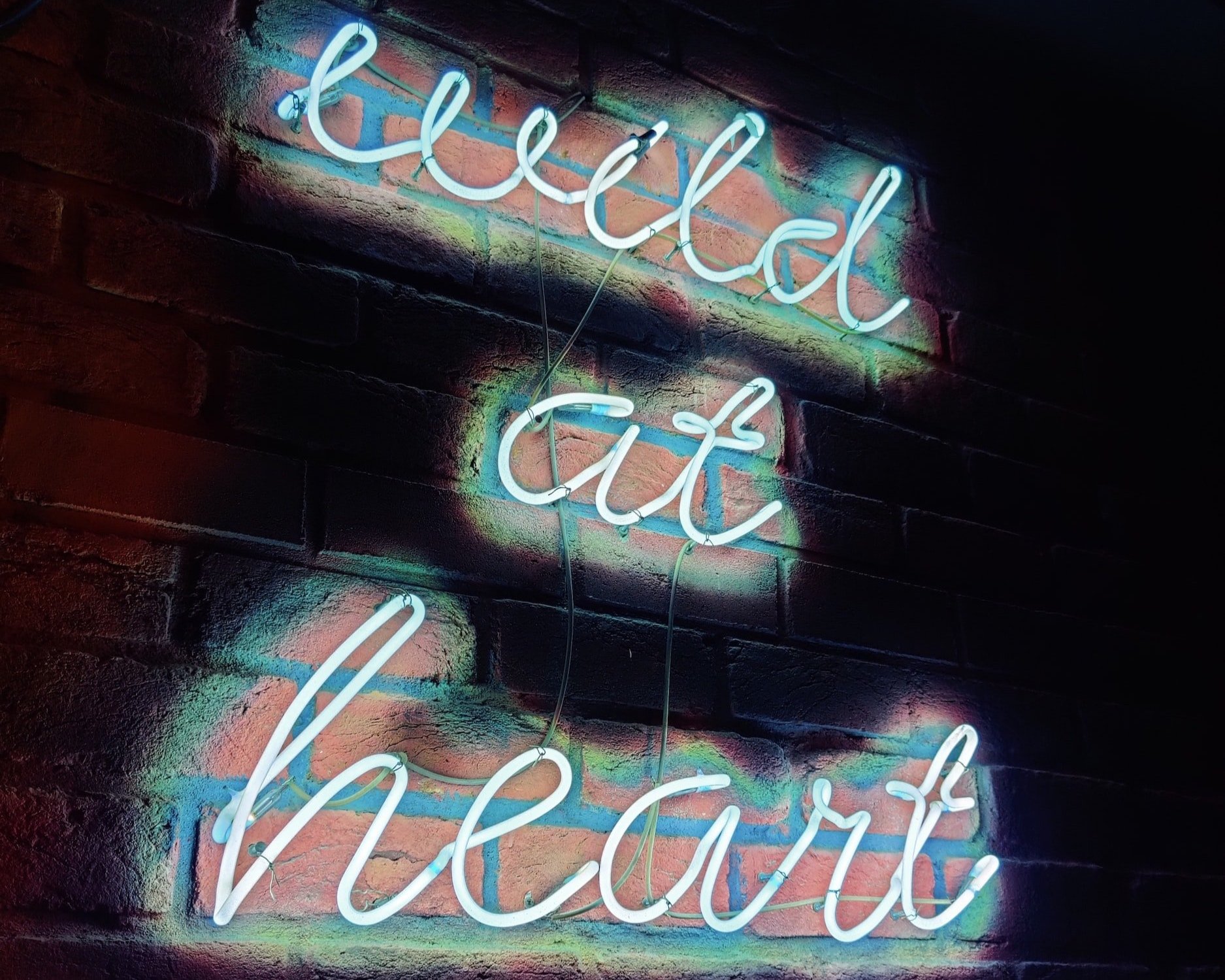 On a brick wall, the words "wild at heart" are displayed in neon.