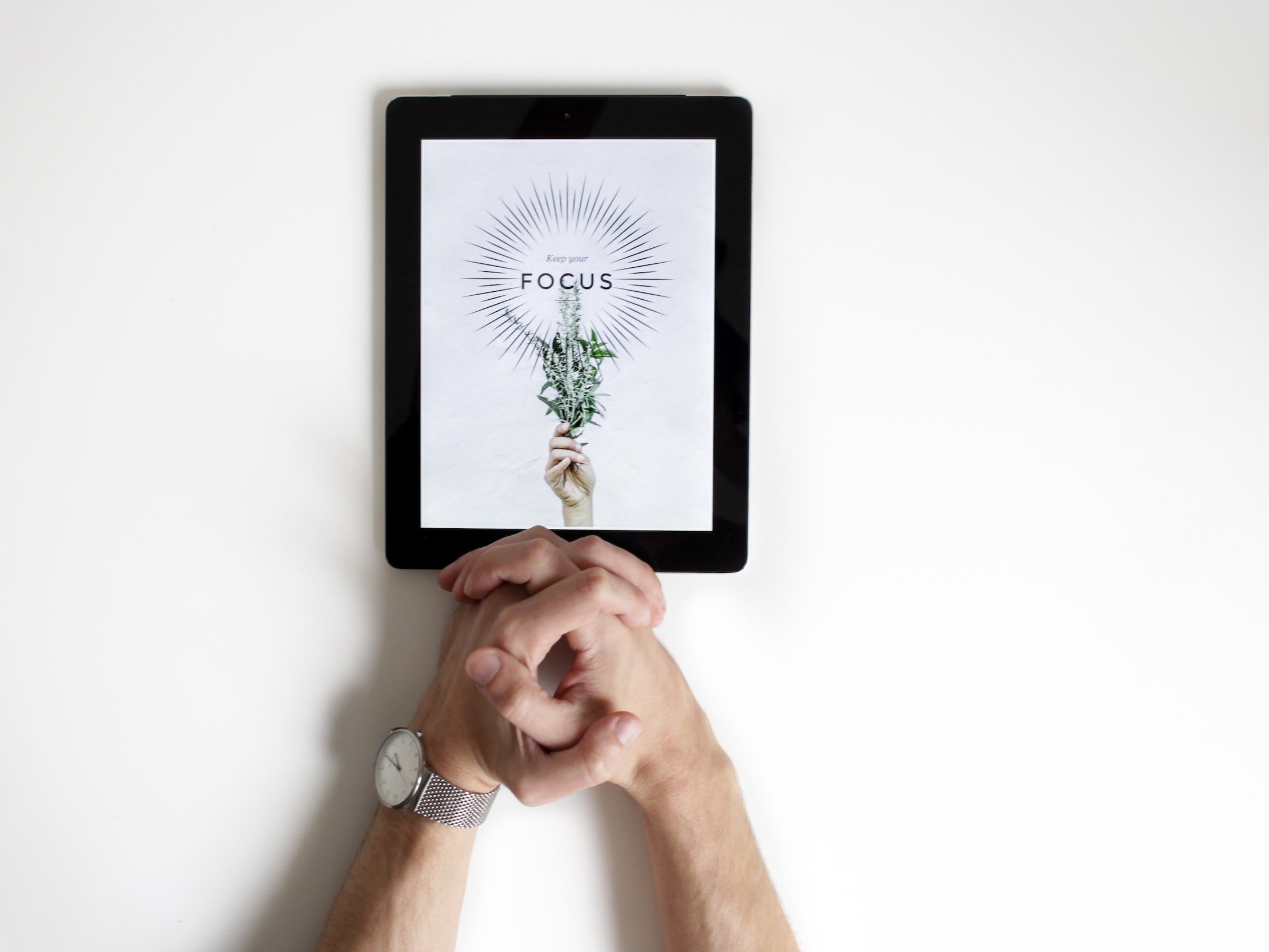 Clasped hands resting on an iPad with the words "Keep your Focus" displayed.