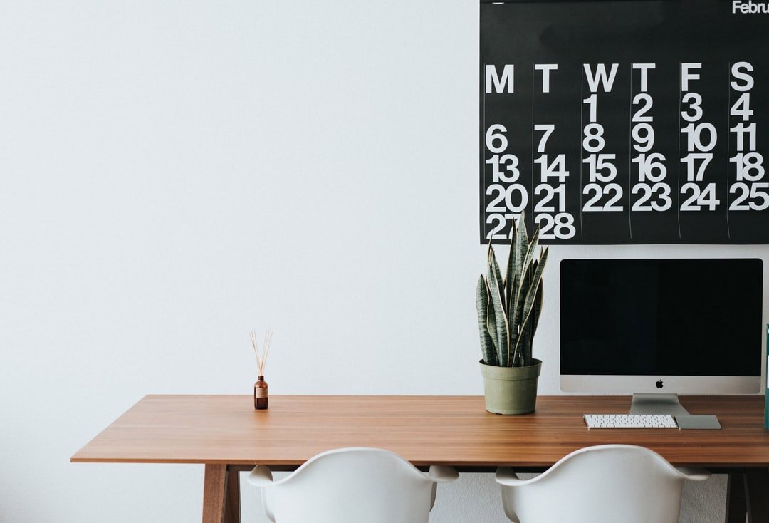 Apple computer on a desk with a calendar hanging above.