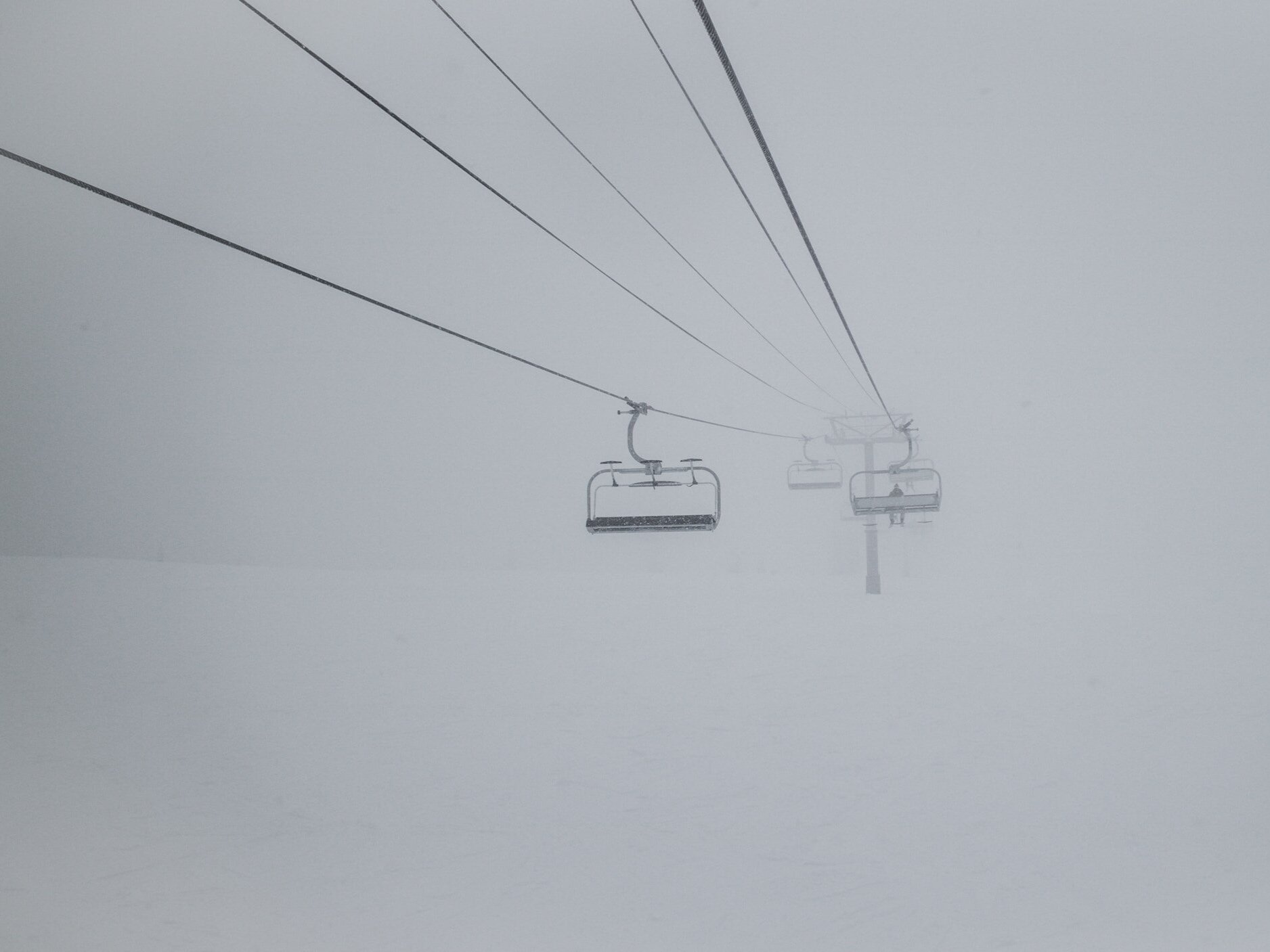 A person is sitting on a ski chair lift in the fog, with very little visibility in front of him.