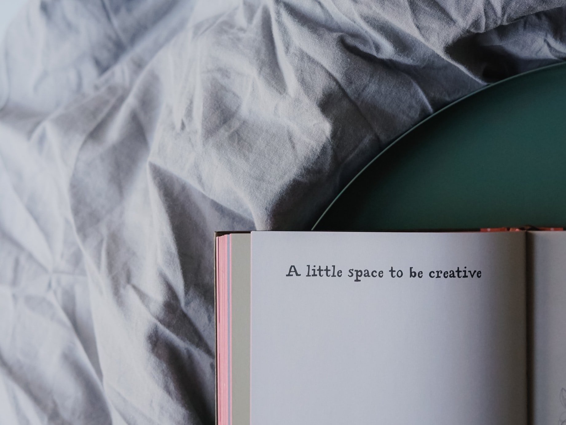 A blank sketch book is laying on a bed cover with the words "A Little Space to be Creative" written out.