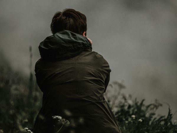 A person sits facing away, deep in thought, looking over a misty field with wildflowers.