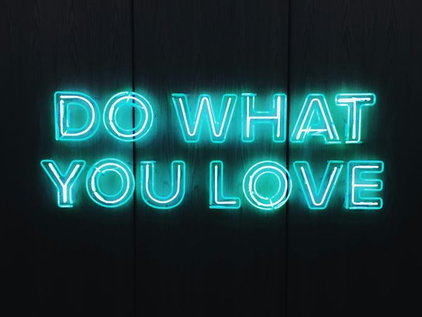 Neon sign reading "Do what you love" against a dark wooden background, encouraging following one's passions.