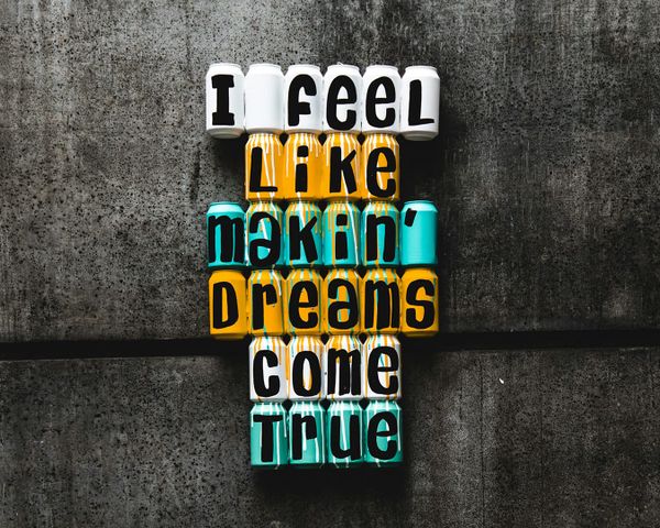 Colourful cans on a grey wall spell "I feel like makin' dreams come true."