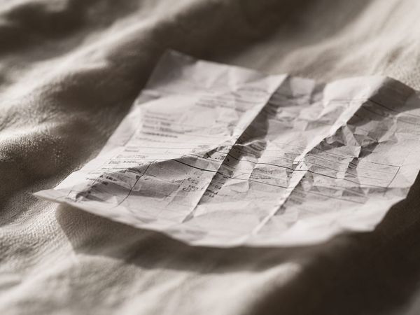 Creased invoice on linen fabric in warm natural window light with shallow depth of field and soft film-like texture.