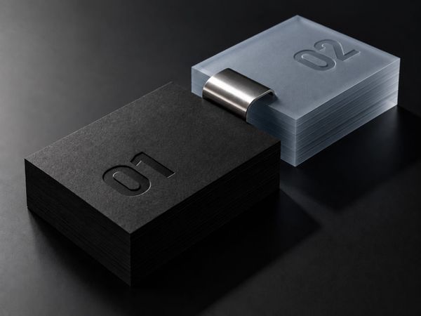 Two stacks of cards embossed 01 and 02, joined by a brushed metal clip. 01 is black and solid, 02 is translucent.