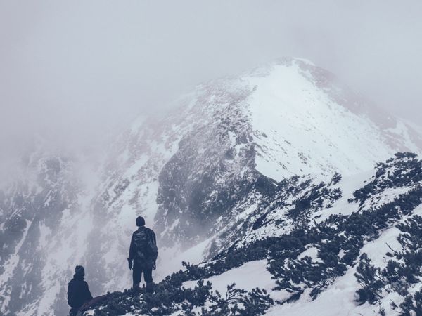 Climbers face imposing snowy mountain, embodying designers' perseverance towards breakthrough achievements.