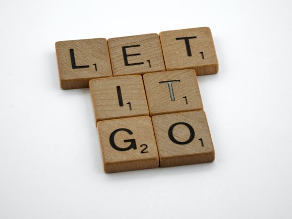 Scrabble tiles arranged to spell 'LET IT GO' on a white background, conveying a message of release and letting go.