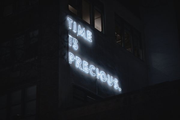 Neon sign on a building reading 'TIME IS PRECIOUS,' highlighting the challenge of finding time for personal design work.