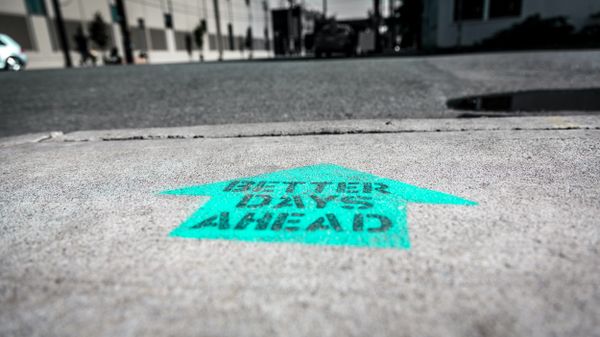 Stenciled message on a city street reading "BETTER DAYS AHEAD" with an arrow, symbolising optimism and progress.