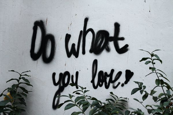 Graffiti "do what you love" on wall with plants, promoting finding fulfillment through pursuing passions in life and work.