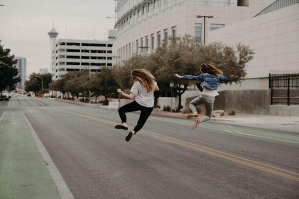 Two women joyfully jumping in the middle of a city street, conveying a sense of freedom and energy.