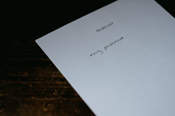 "To Do List" on a paper with the only item written: "mainly procrastinate..." on a dark table.