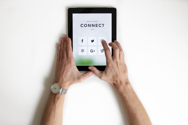 Hands holding a tablet displaying social media icons on a "CONNECT" screen, symbolising reconnection.