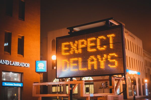 Roadside electronic sign reads "EXPECT DELAYS" at night, symbolising a need for change.