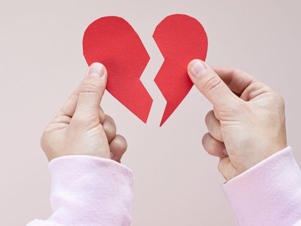 Two hands holding up halves of a broken paper heart, symbolising the danger of becoming too attached to your creative work.