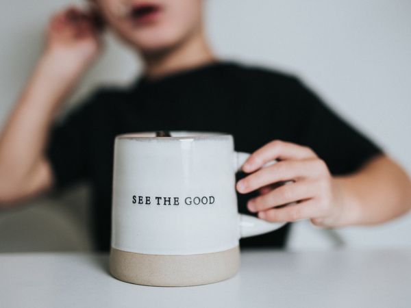 Person holding mug with "See the Good" printed on it, suggesting an outlook of positive thinking and gratitude.