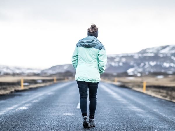Person in mint green jacket walking on road amid snowy mountains, representing a journey or new path.