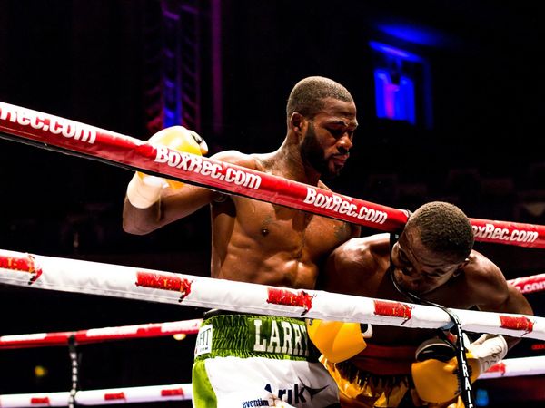 Two men engaged in a boxing match, one with his head between the ropes.