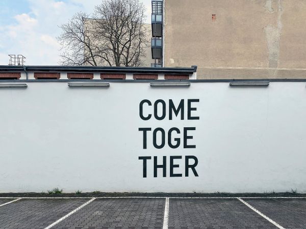 On a large white wall in a car park, the words "Come Together" are painted in black.