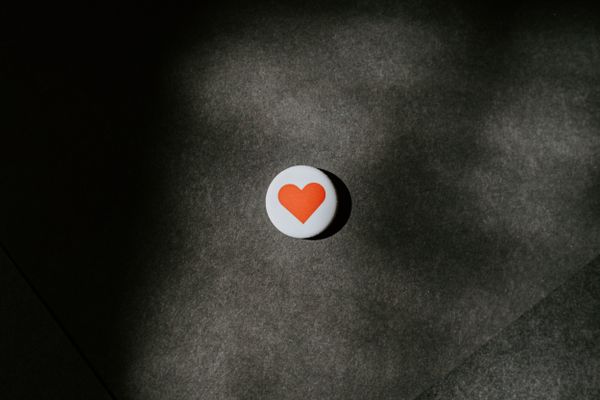 On a felt surface, a white badge with a single red love heart is displayed.