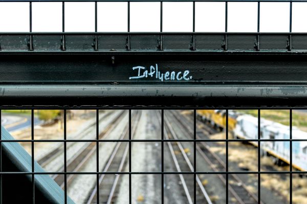 "Influence" written in white on a black fence over a railway track.