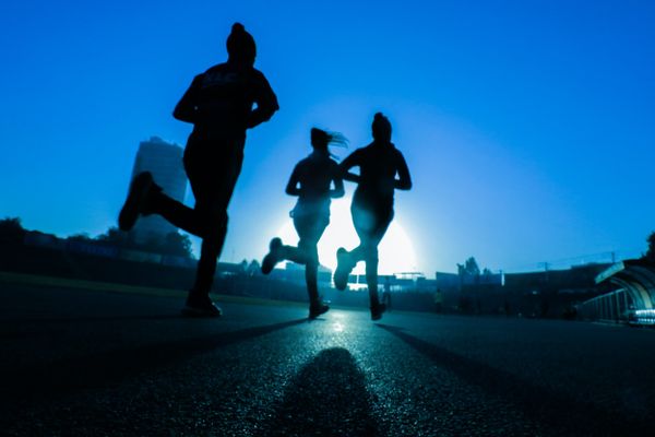 Silhouettes of three joggers at dawn under clear blue sky, symbolizing healthy, active lifestyle.