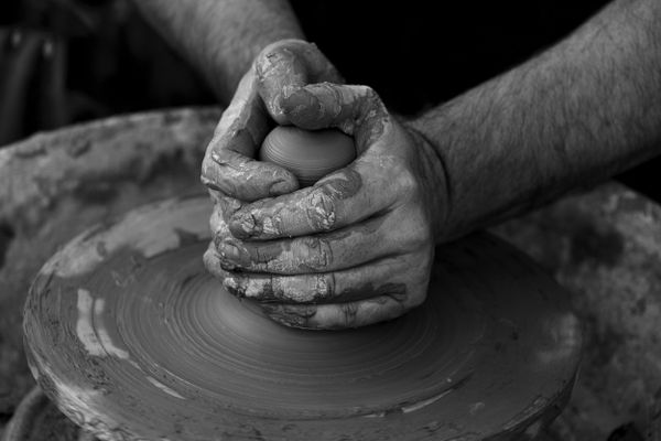 Black and white image of a potter's clay-covered hands shaping a vessel on a spinning pottery wheel.