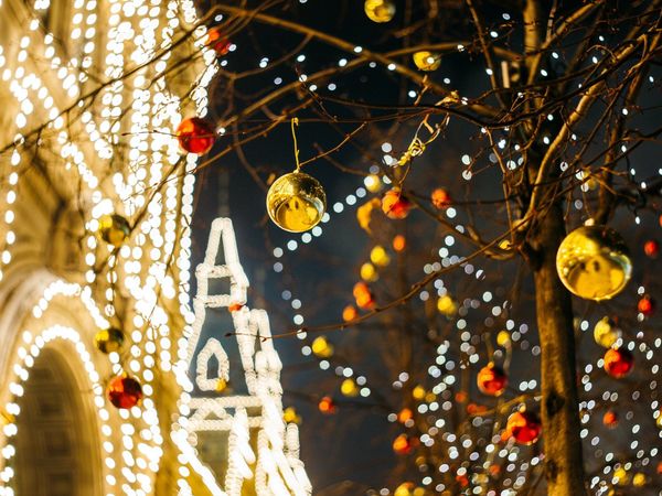 Illuminated Christmas decorations on bare tree branches at night with out-of-focus lights in the background.