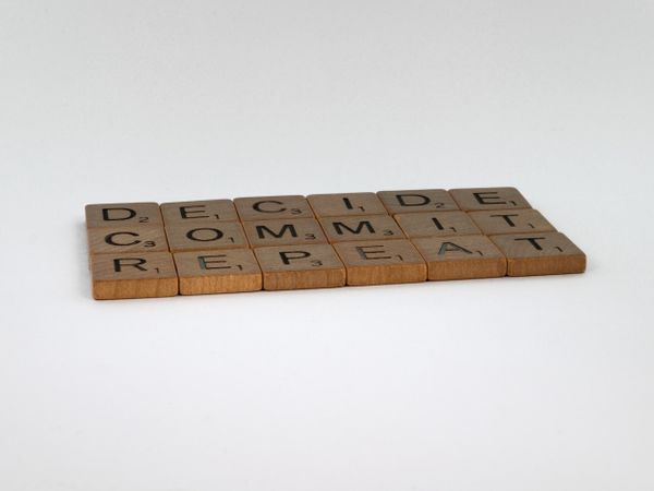 In wooden letter tiles, the words "Decide, Commit, and Repeat" are written.