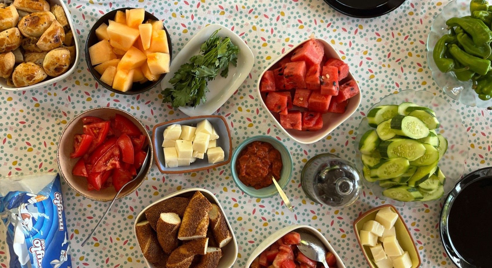 Breakfast table with assorted breads, cut-up vegetables, dips, olives, cheeses.