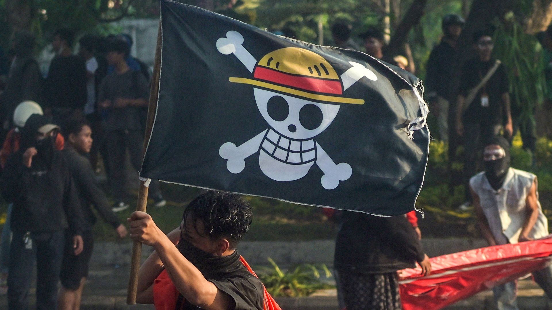 Bir protestocu, Surabaya'da düzenlenen protesto esnasında Endonezya ulusal bayrağını ve One Piece'den korsan bayrağını taşıyo