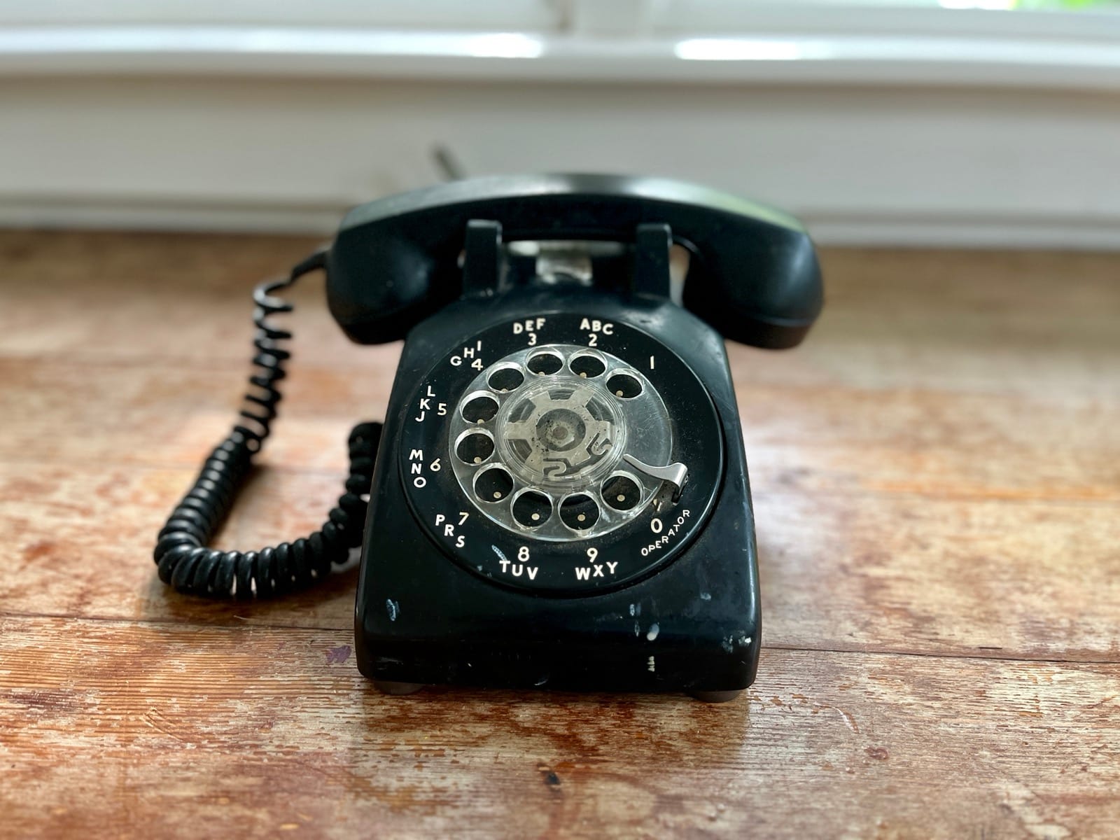 A distinguished black rotary phone on a wooden floor.