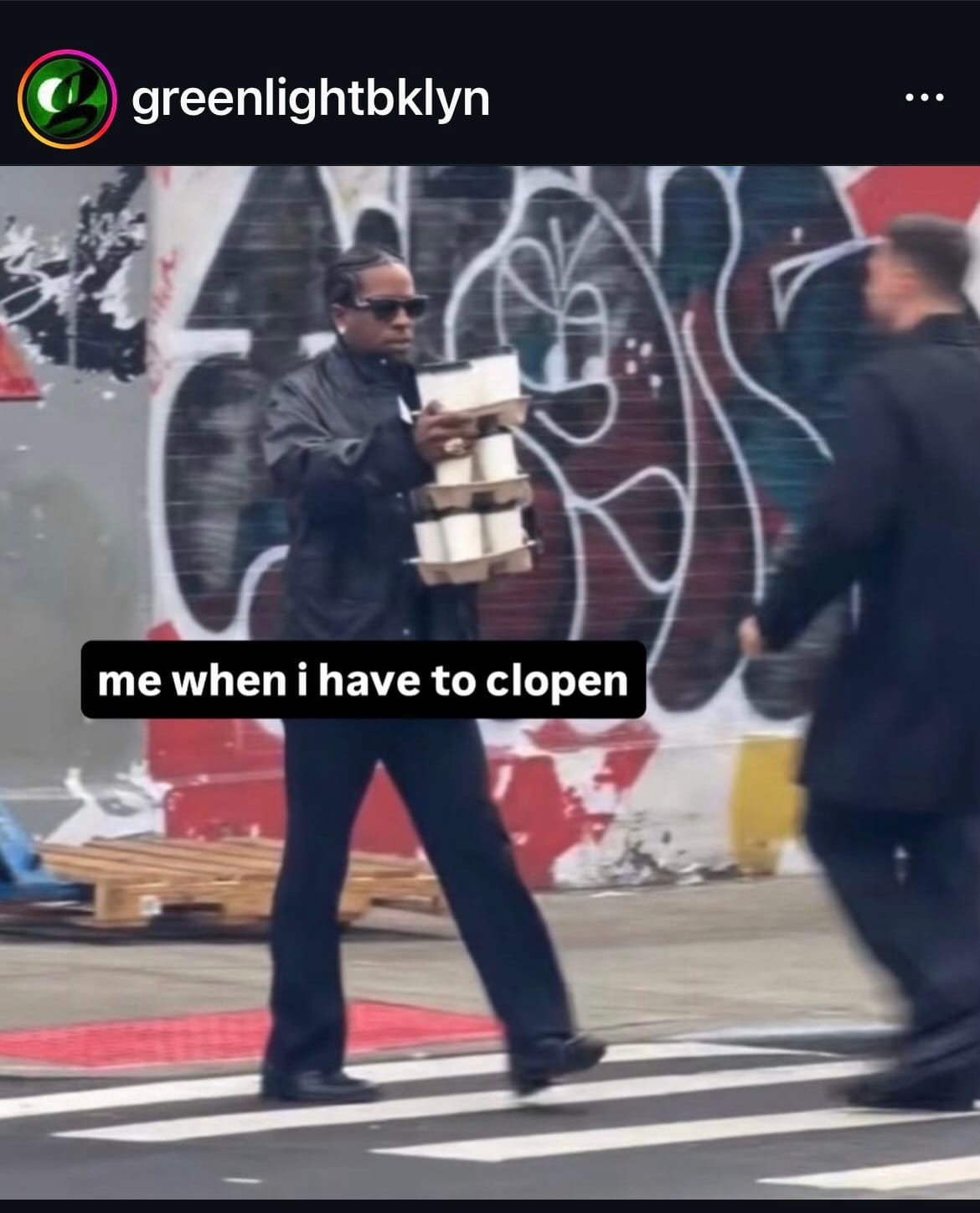 A screenshot of a meme made by the bookstore Greenlight Brooklyn, featuring a person holding several stacks of coffee cups walking down a NYC street with the caption: "me when i have to clopen"
