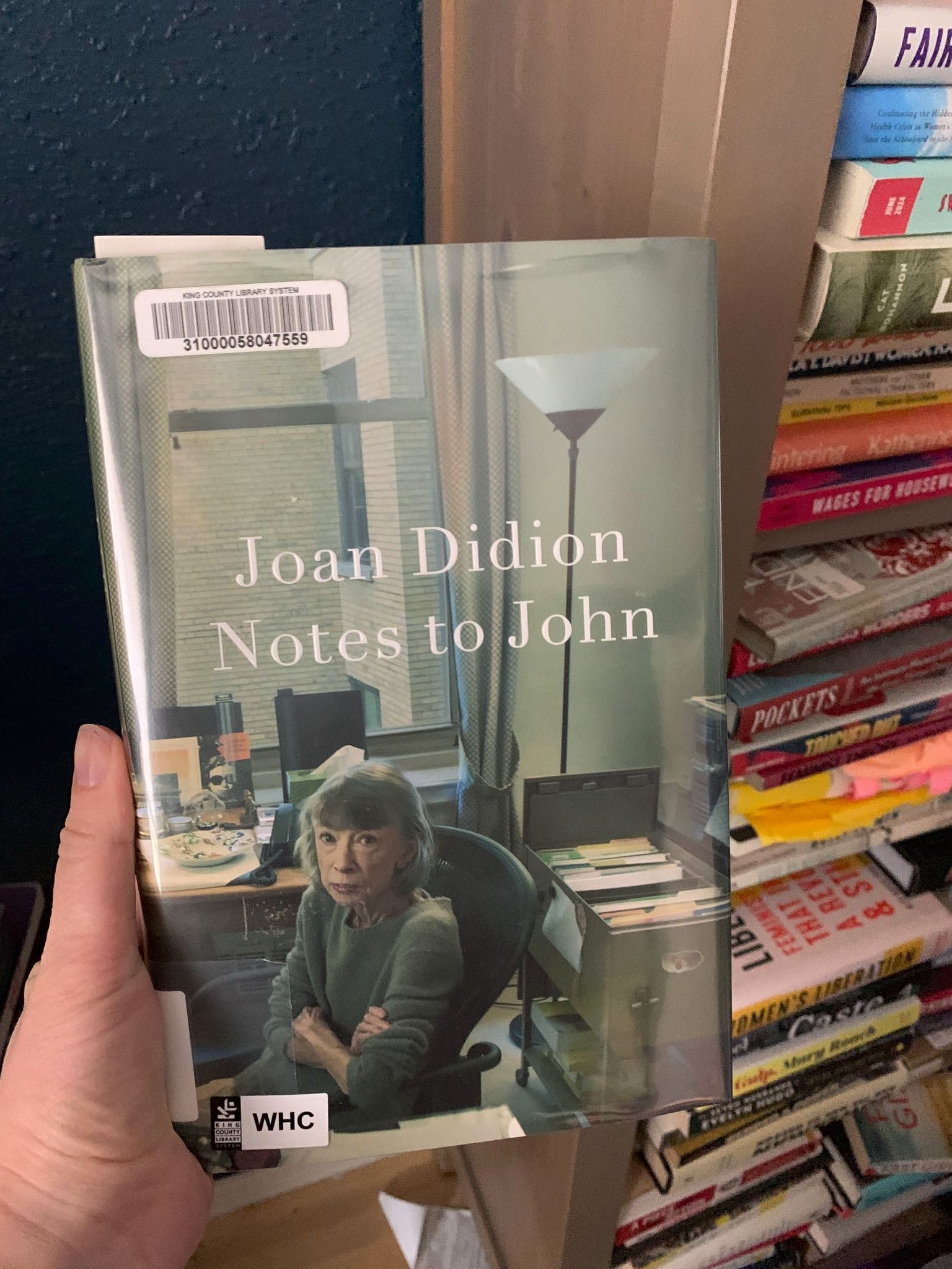 Close-up of a person's hand holding Didion's "Notes to John," in which the author can be seen in the bottom half with her arms folded.