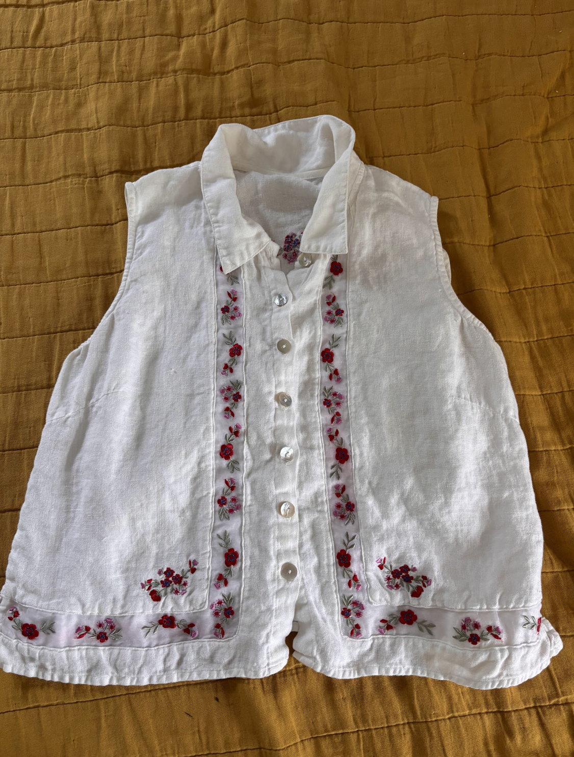 A white, sleeveless, button-down top with embroidery flowers running the length of its middle and bottom.