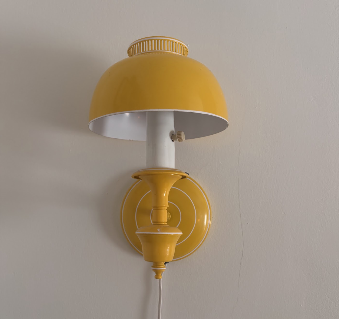 A yellow, retro sconce lamp with a domed top on a white wall.