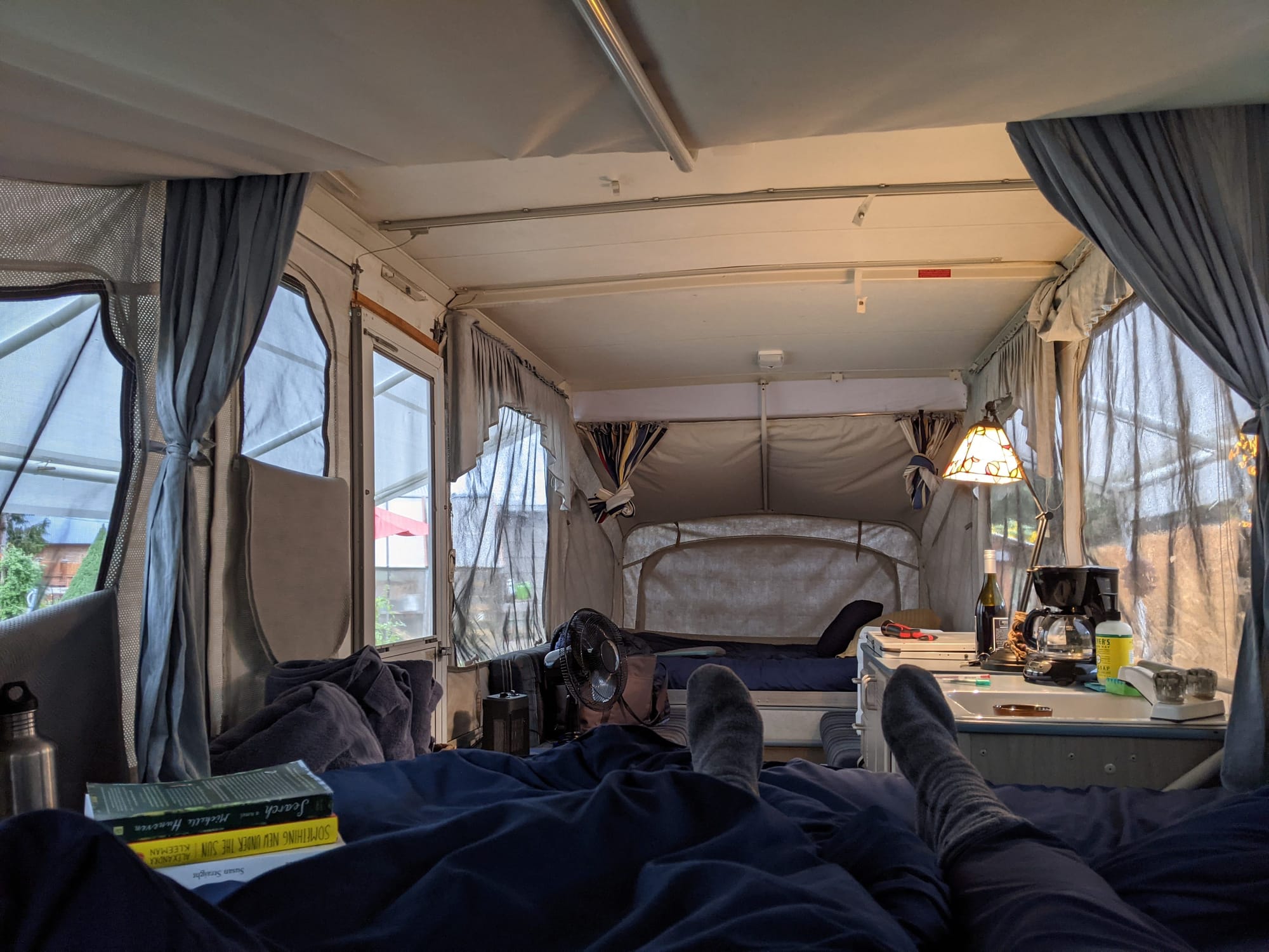 Photo from inside an RV taking by Lydia. The space is sparsely decorated. A pile of books is in foreground with a sleeping area seen in the distance.