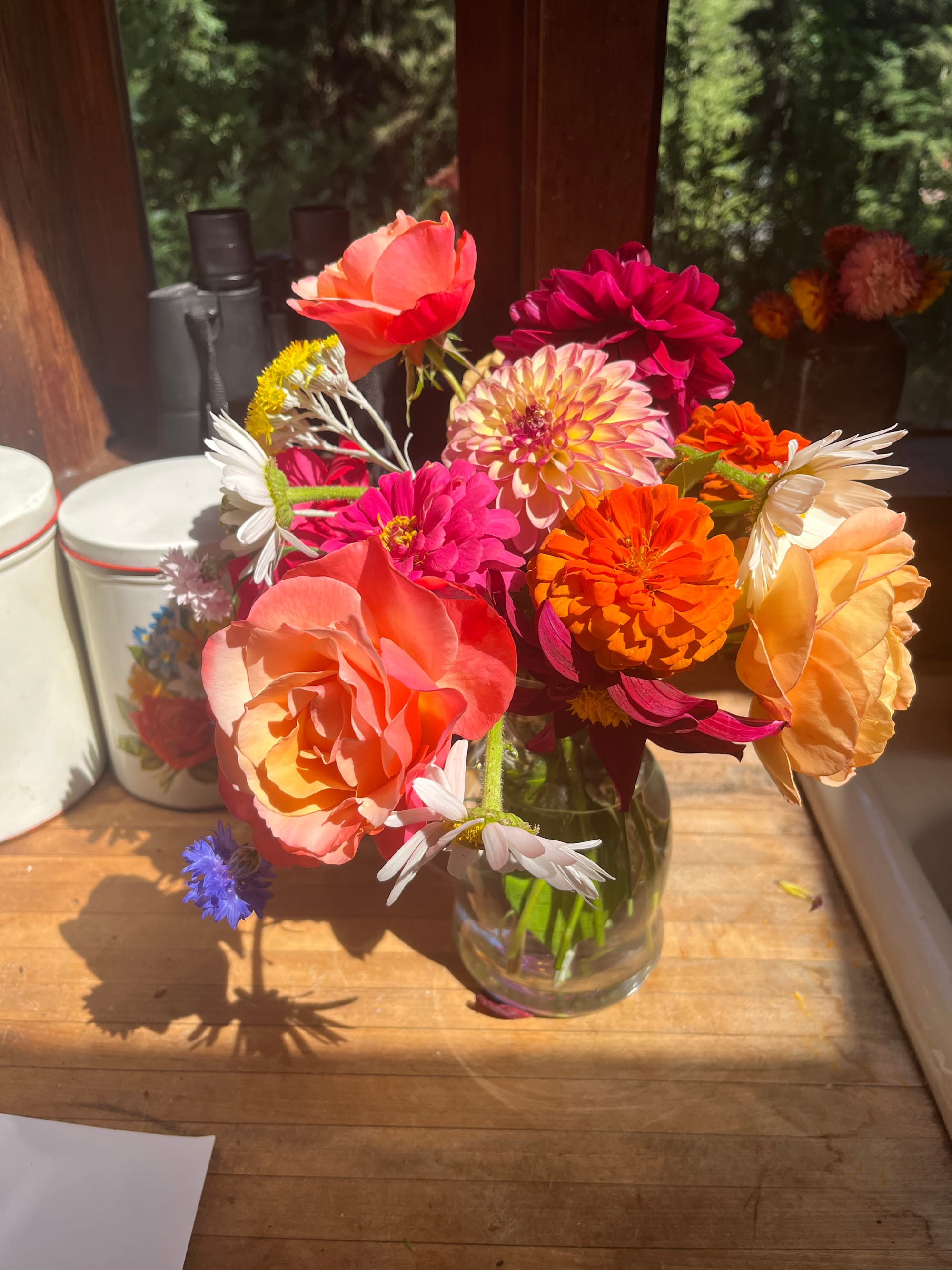 clear vase filled with fuschia, orange, yellow, and white blooms set juxtaposed against a wooden countertop