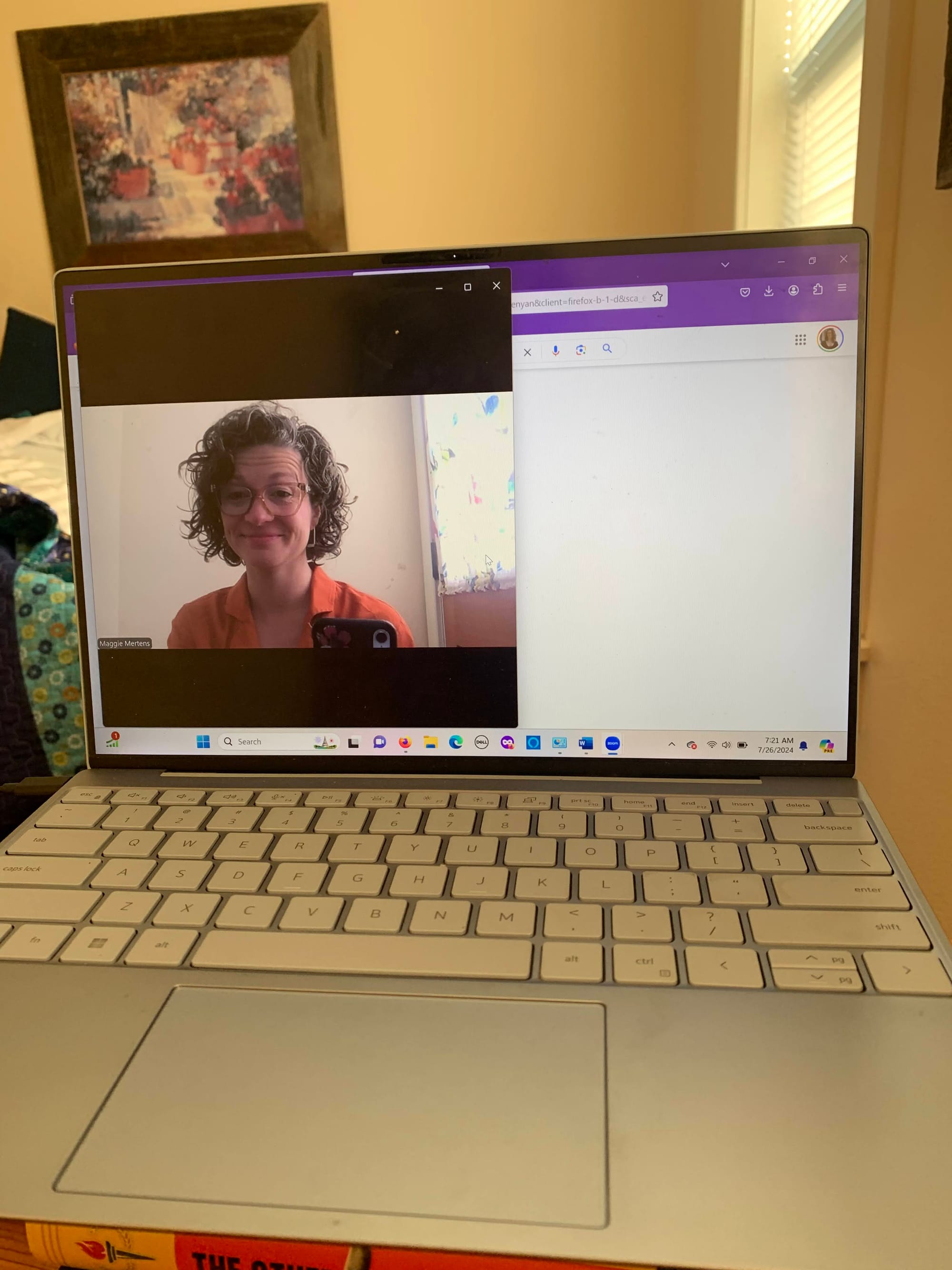 an open laptop with a Zoom screen open showing a woman with curly hair smiling at the camera