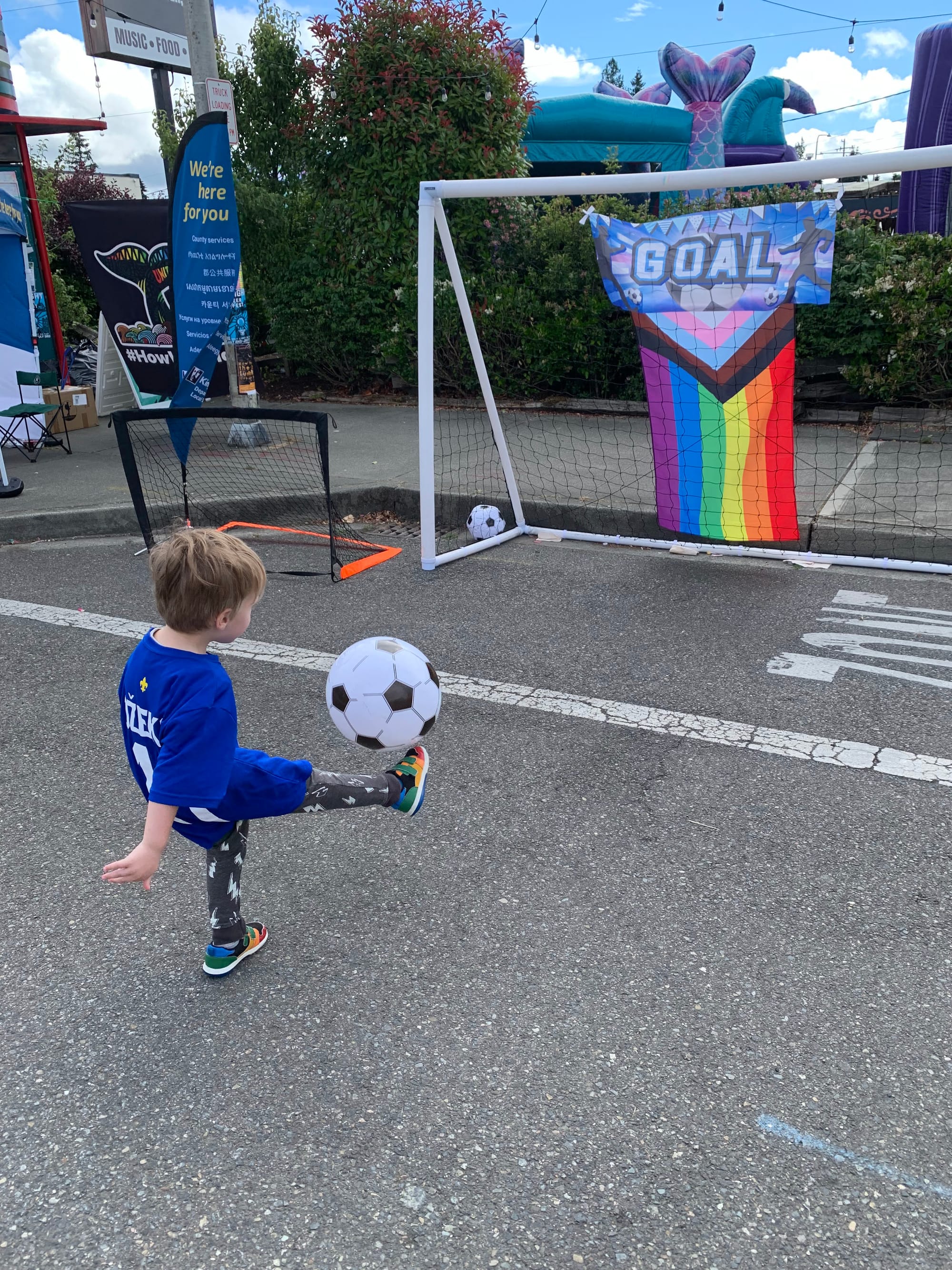 Image of a small child wearing a blue jersey kicking a black-and-white soccer ball towards a goal
