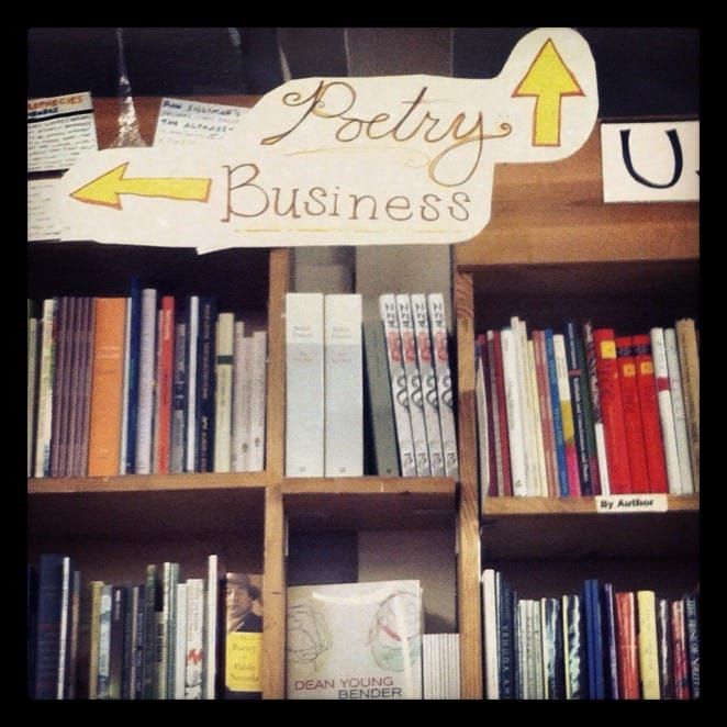 A photo of bookshelves inside Green Apple Books. A sign on top reads "Poetry" and "Business," and has the arrows pointing in different directions.