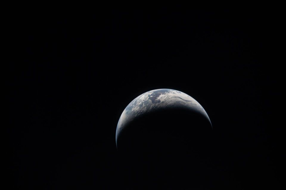 a photograph of earth from the Artemis mission, black background adn a crescent of earth: blue, green and white clouds are visible.